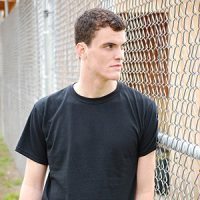 Angry teenage boy staring through a chain link fence